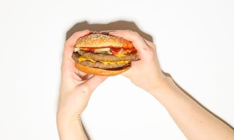 Photo d'un hamburger tenu par quelqu'un sur fond blanc